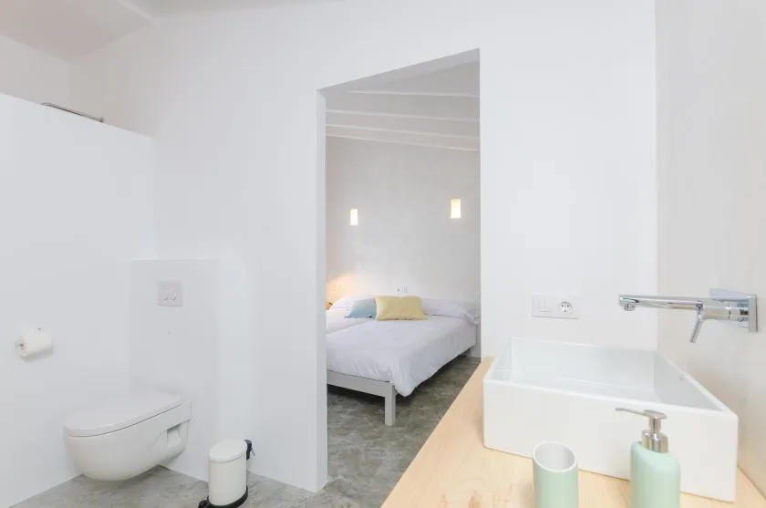 A bright bathroom with a sink and a bedroom visible through the doorway.