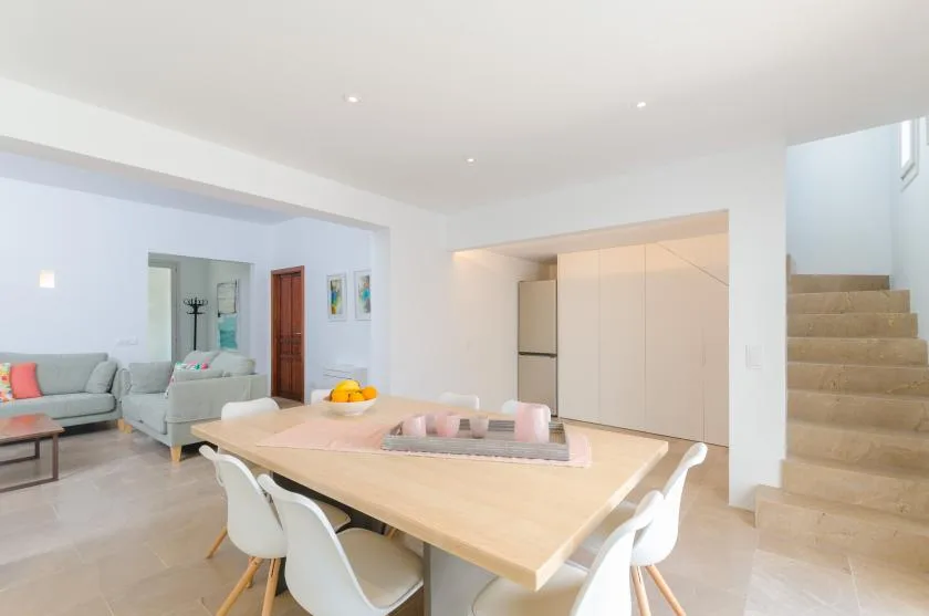 A bright dining area with a large table and white seating beside a staircase.