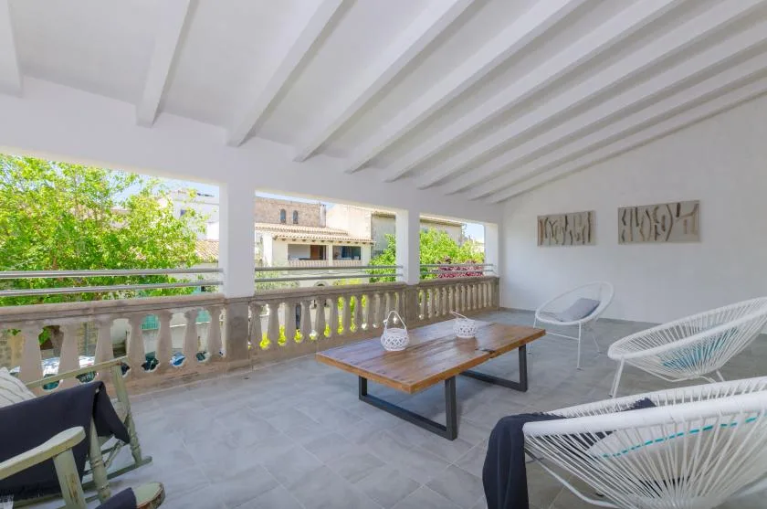 A covered terrace with woven seating and a wooden table overlooks leafy surroundings.