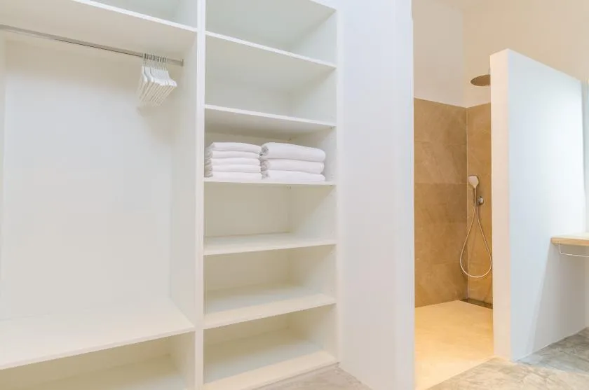 A bathroom with open shelving, folded towels, and a shower.