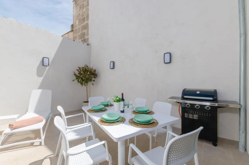 An outdoor dining area with a set table and a grill against the wall.