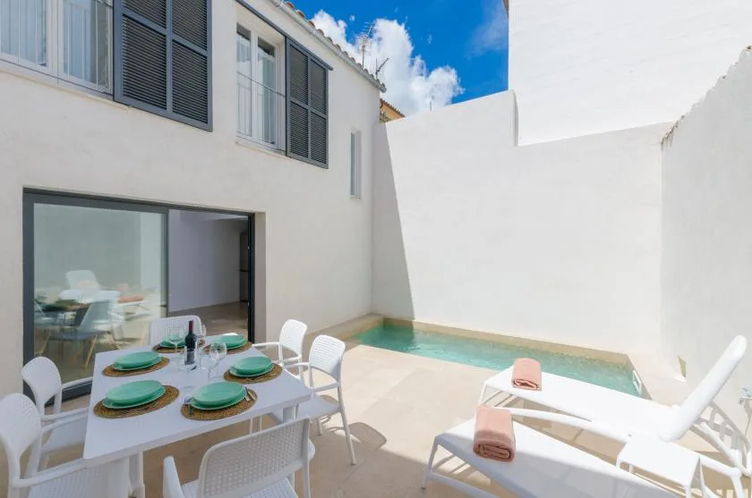 A sunlit patio with a dining table and a small pool beside the house.
