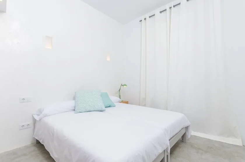 A bright bedroom with a white bed and floor-length curtains.