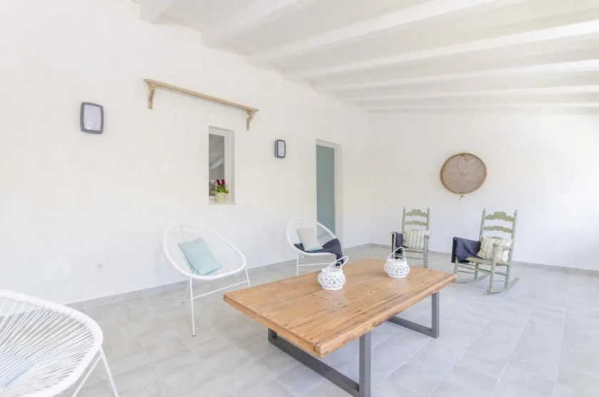 A bright covered patio with a wooden table and white seating.