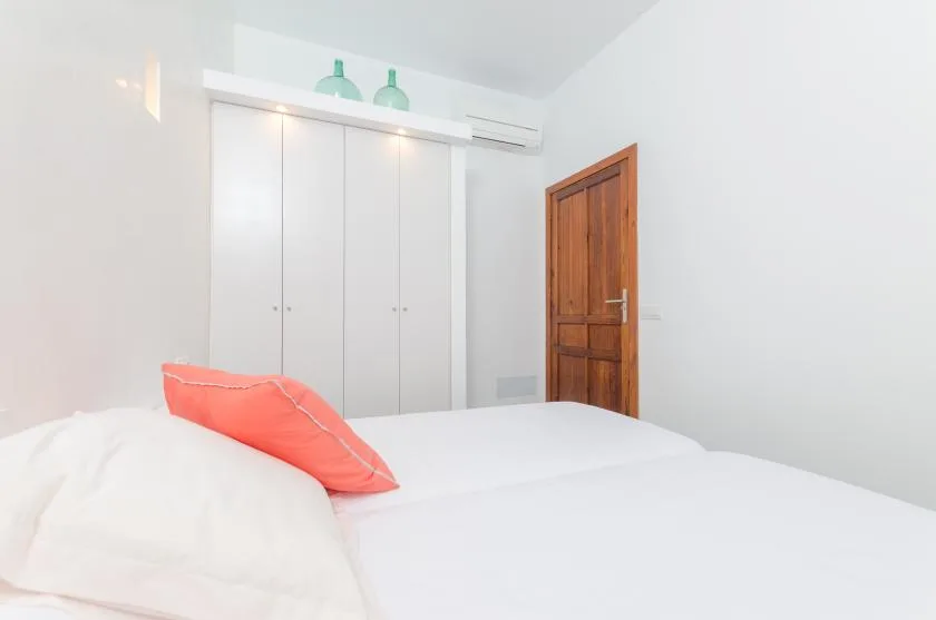 A bright bedroom with white bedding and a coral accent pillow.