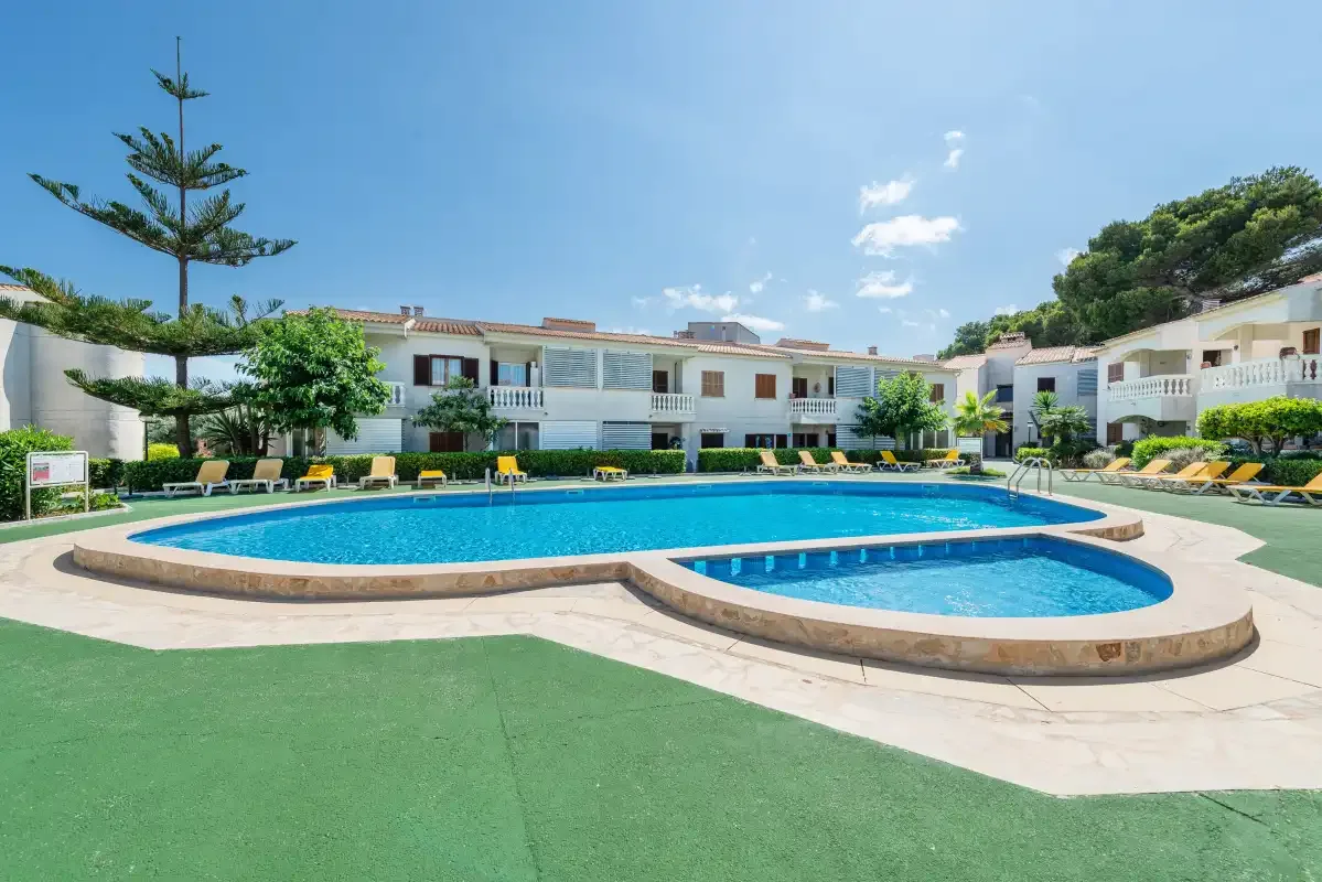 A swimming pool and smaller adjoining pool sit in front of a row of buildings.