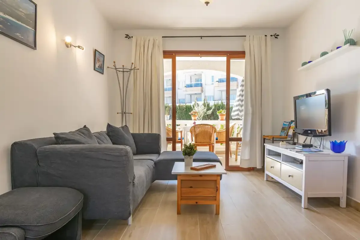 A living room with seating, a television, and glass doors opening onto a balcony.