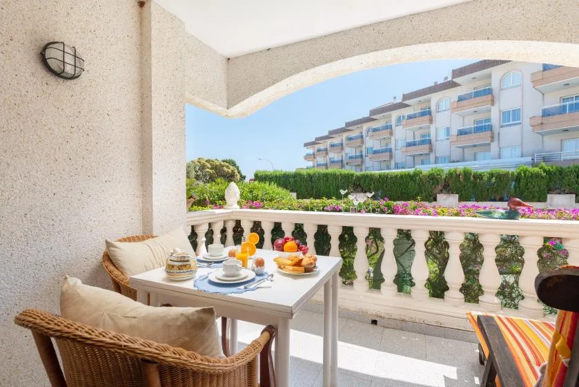 A balcony seating area with a set table overlooking gardens and nearby buildings.