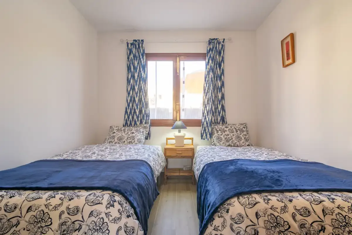 A bedroom with two single beds and a window between patterned curtains.