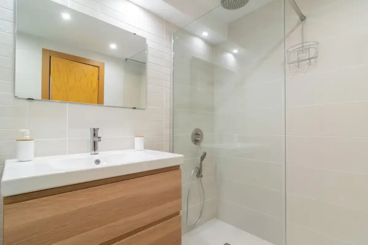 A bright bathroom with a sink, mirror, and glass shower.