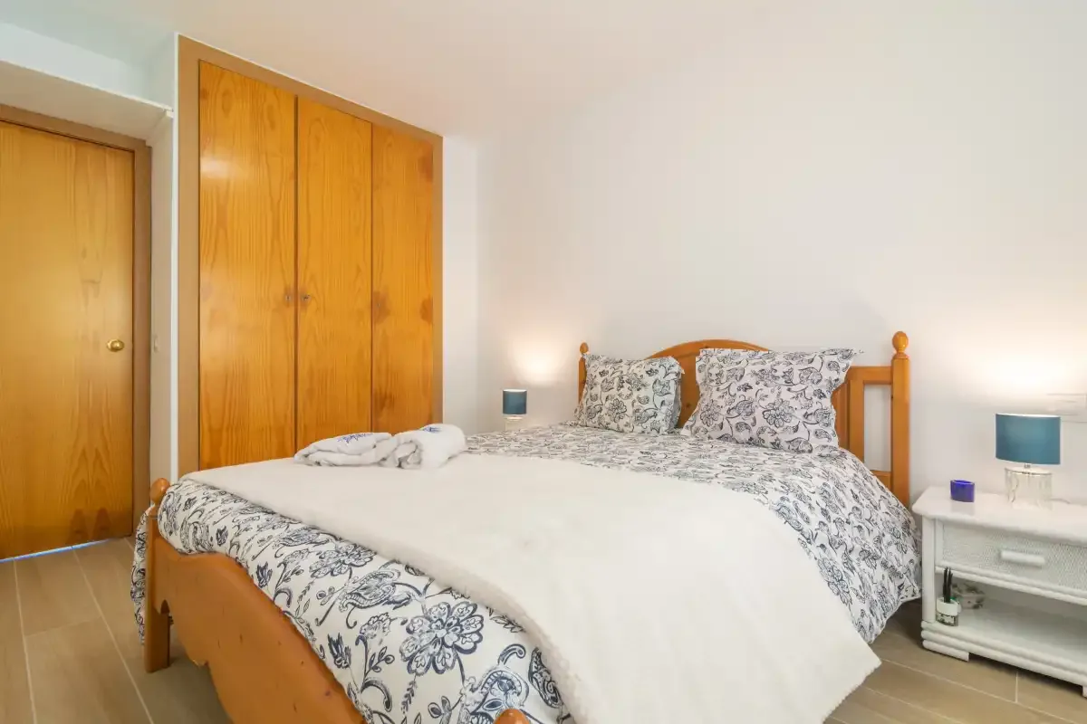 A bedroom with a wooden bed, patterned bedding, and built-in wardrobes.
