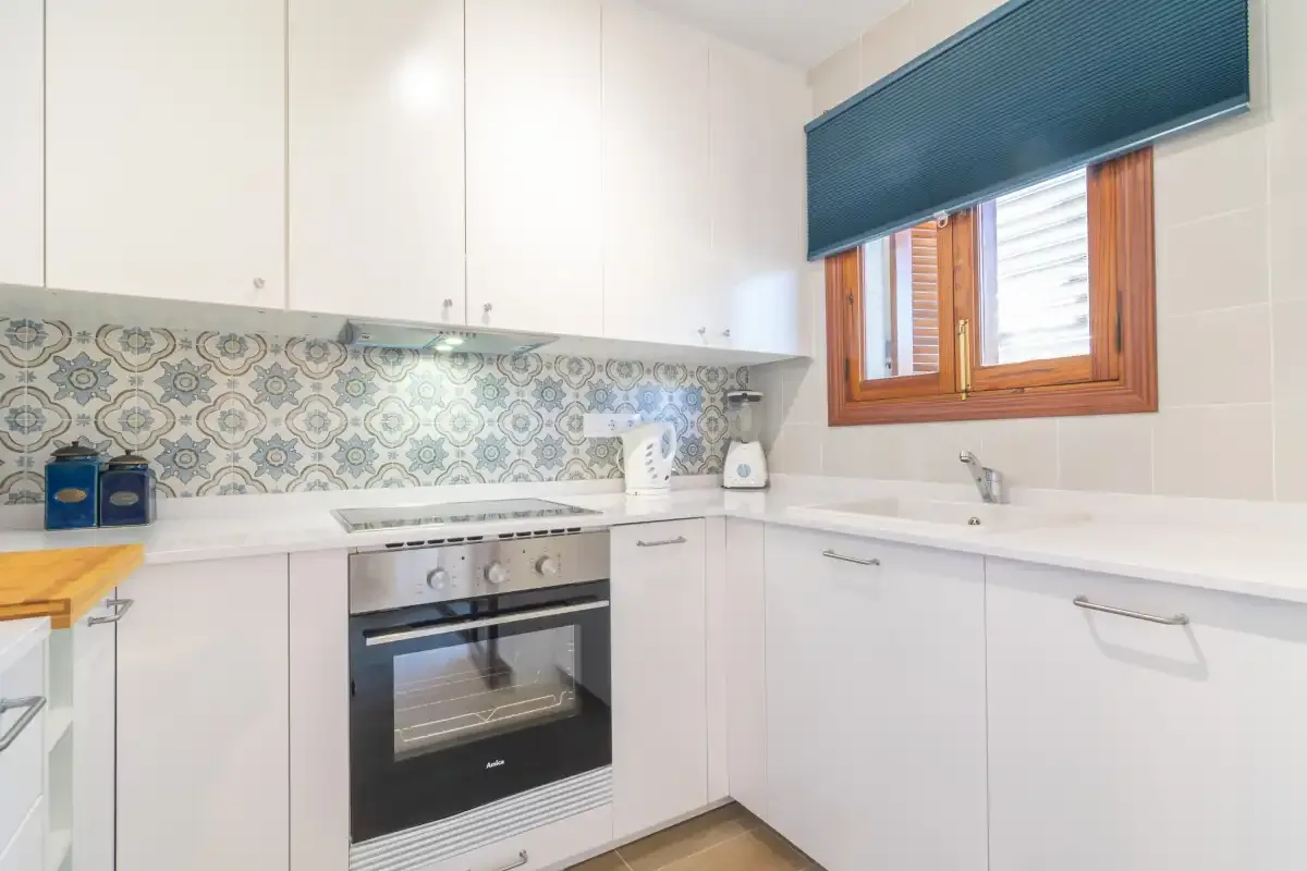 A bright kitchen with white cabinets, a built-in oven, and a window.