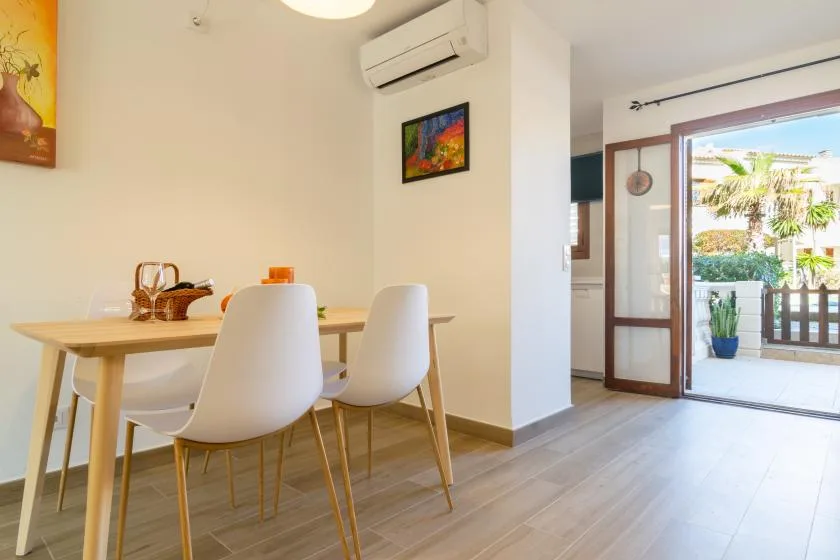 A dining area with a wooden table and white seating beside an open patio door.