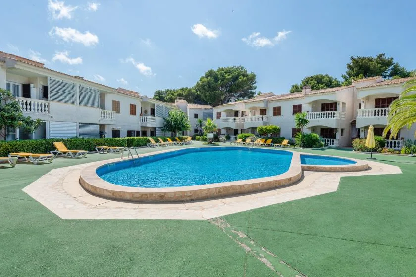 An outdoor swimming pool is surrounded by low-rise buildings and lounge seating.