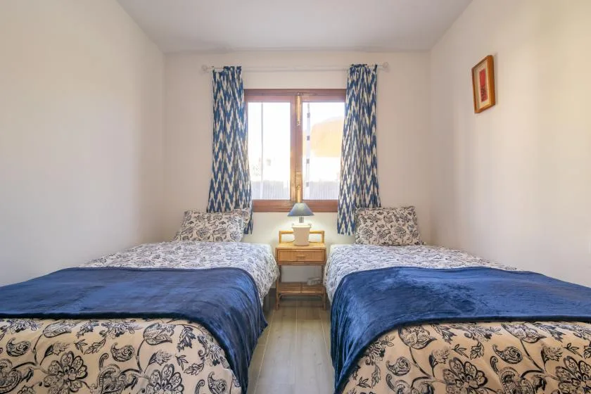 A bedroom with two beds, a small bedside table, and a window with patterned curtains.
