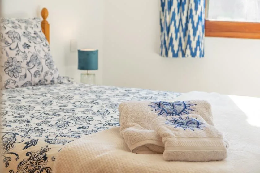 A bedroom with patterned bedding and folded towels on the bed.