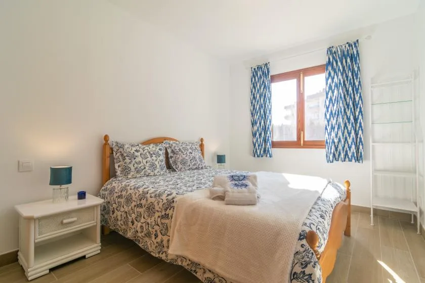 A bedroom with a patterned bedspread, blue curtains, and a window.