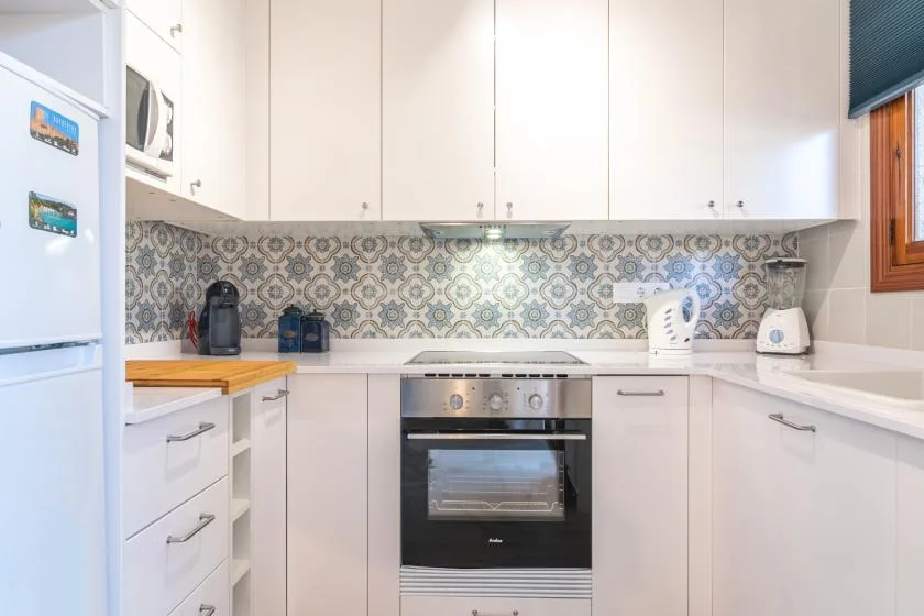 A bright kitchen with white cabinets, an oven, and patterned backsplash.