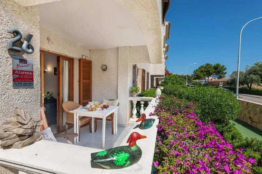 A covered patio with a small dining table overlooks a flower garden.