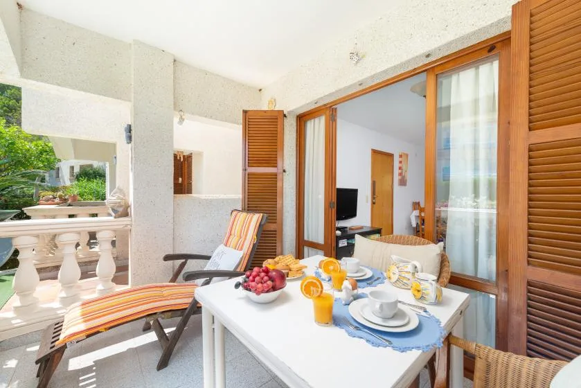A furnished terrace with a dining table and seating beside open wooden shutters.