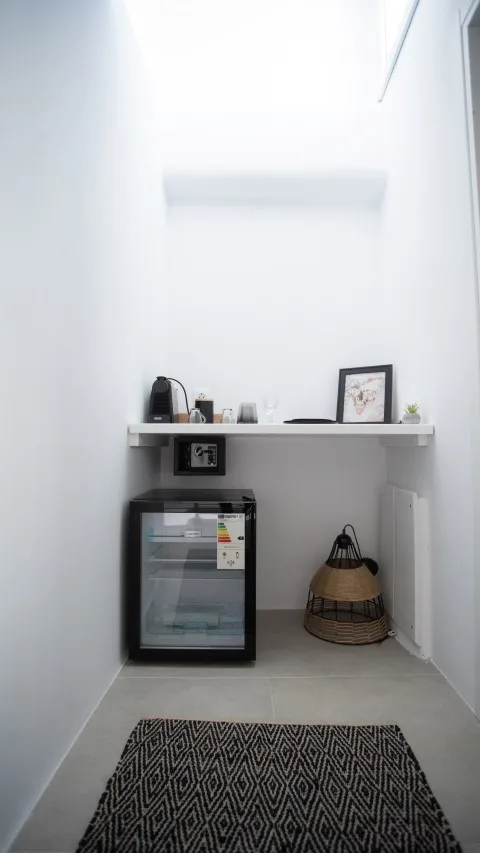 Una pequeña zona de refrigerios tiene un refrigerador bajo una repisa estrecha.