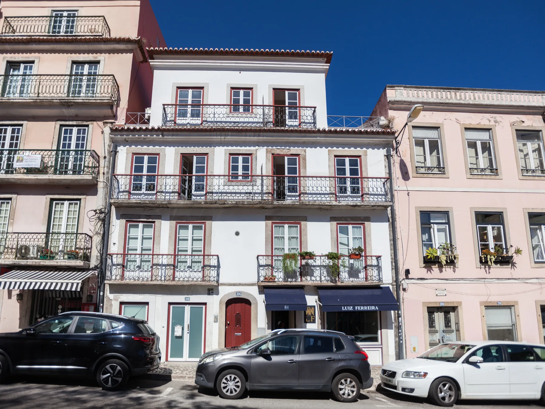 Una hilera de edificios urbanos con balcones y coches estacionados en la calle.
