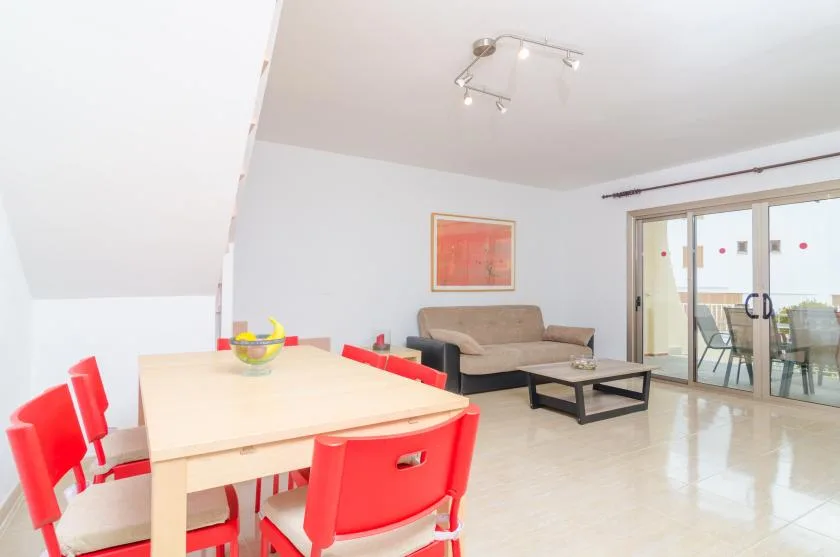 A bright living and dining area with red dining chairs and a seating area.