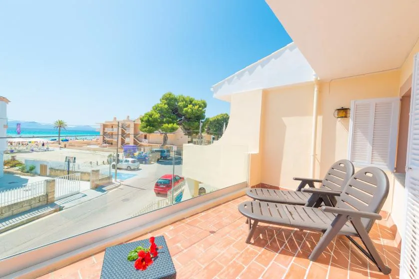 A sunny balcony with seating overlooks a beachfront pool and the sea.