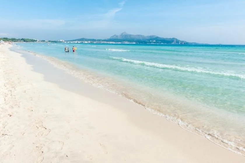 A sandy beach borders clear turquoise water beneath a blue sky.