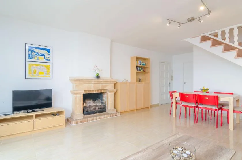 A bright living and dining area with a fireplace, television, and red dining chairs.