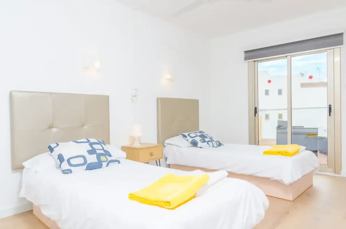 A bright bedroom with two beds and folded yellow towels.