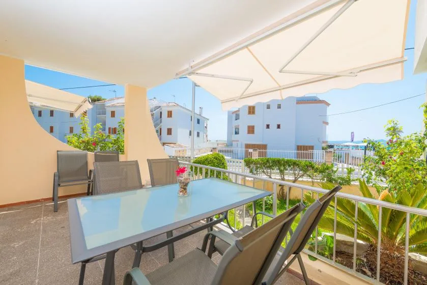 A covered outdoor terrace has a glass-top table, seating, and views of nearby buildings.