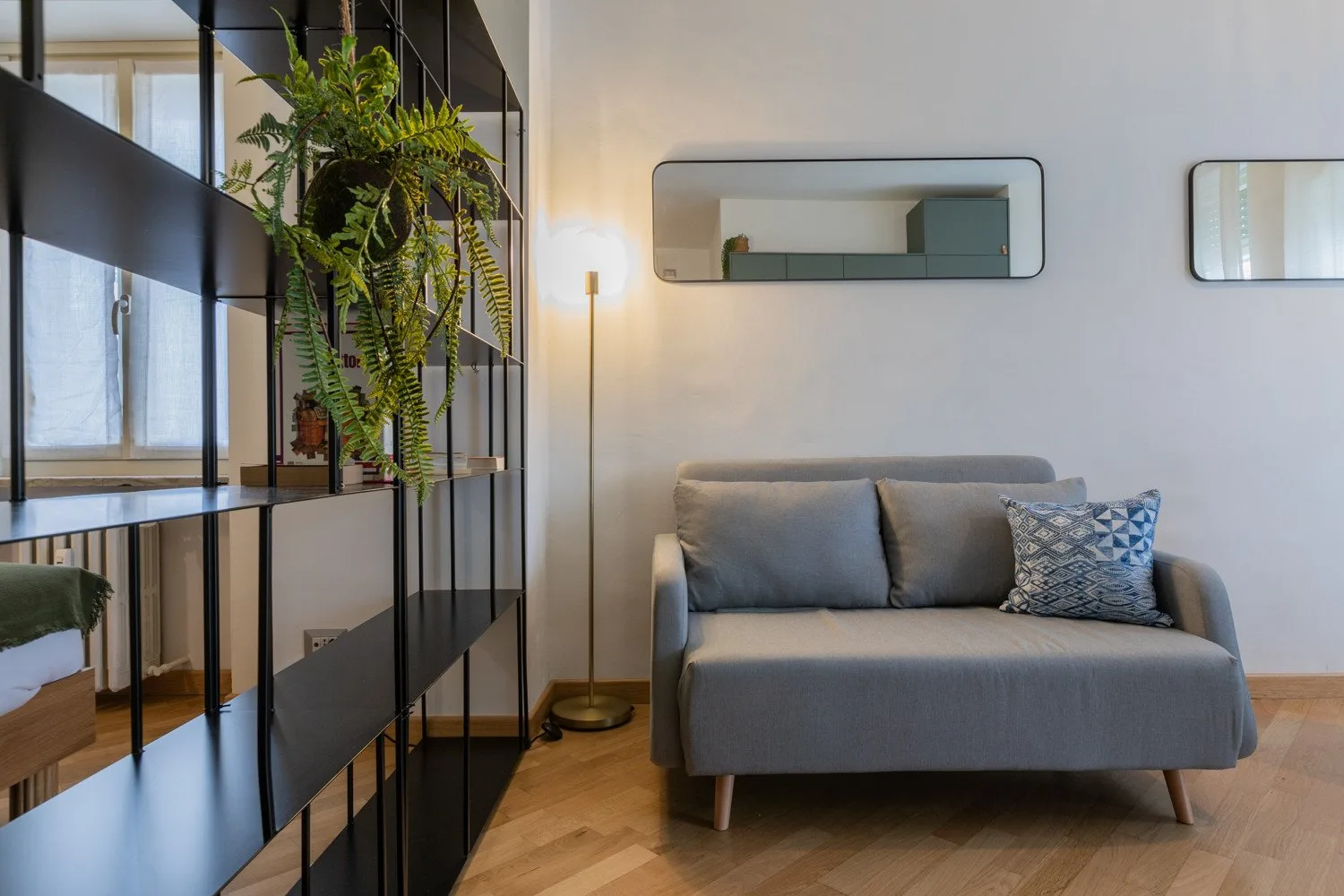 A living area with gray seating, a wall mirror, and a tall plant.