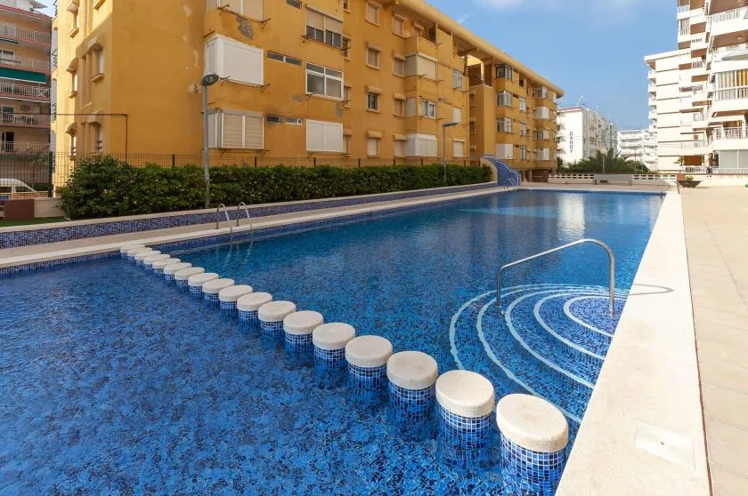 An outdoor swimming pool beside apartment buildings, with steps leading into the water.