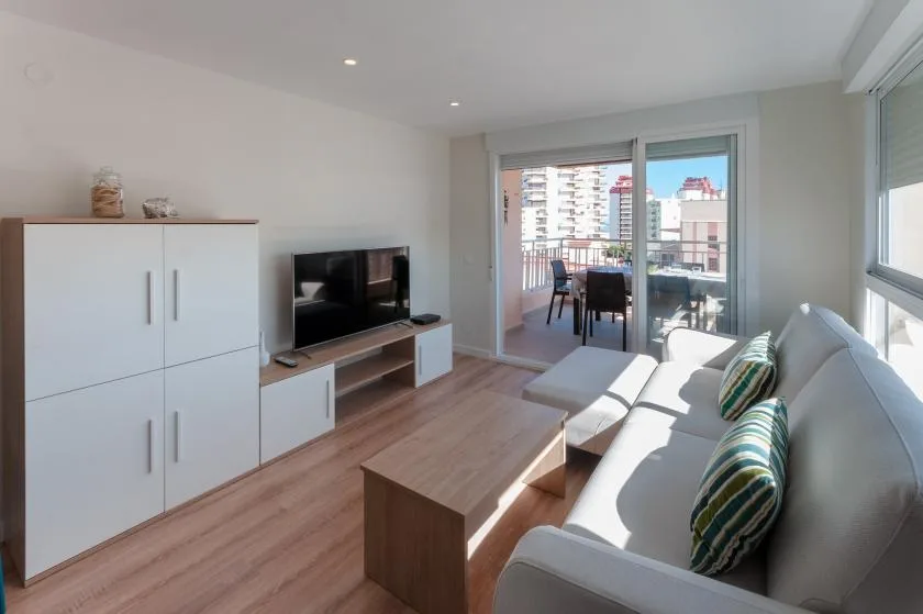 A bright living room with seating, a television, and glass doors opening onto a balcony.