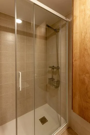 A tiled bathroom shower with glass panels and a handheld showerhead.