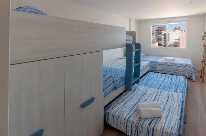 A bedroom with blue-striped beds and a window overlooking nearby buildings.