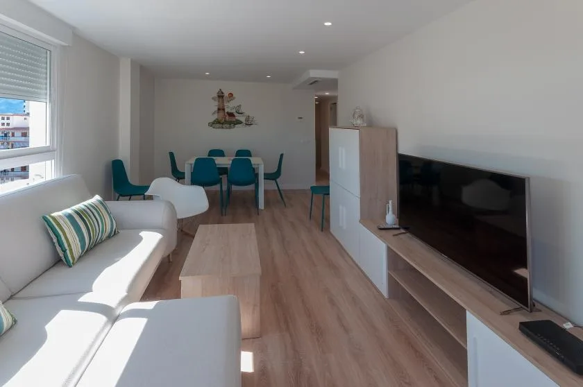 A bright living and dining area with seating, a table, and a television.