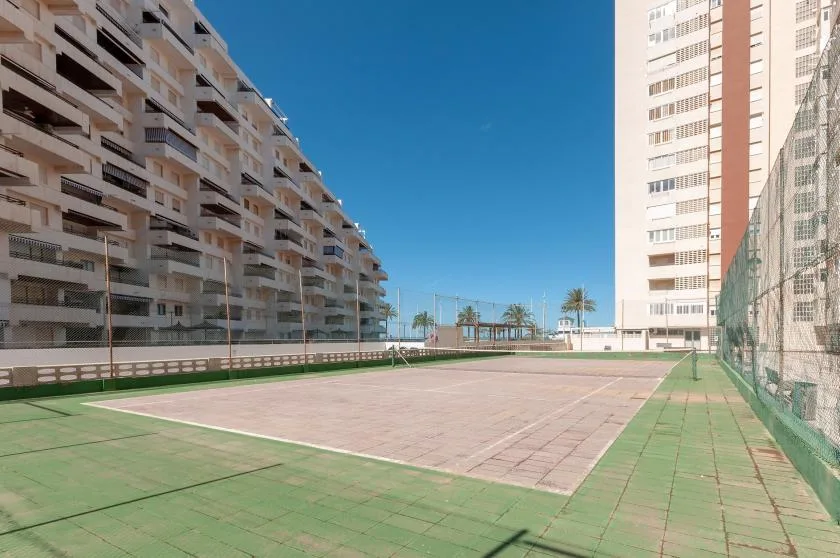An outdoor sports court sits between tall apartment buildings under a clear sky.