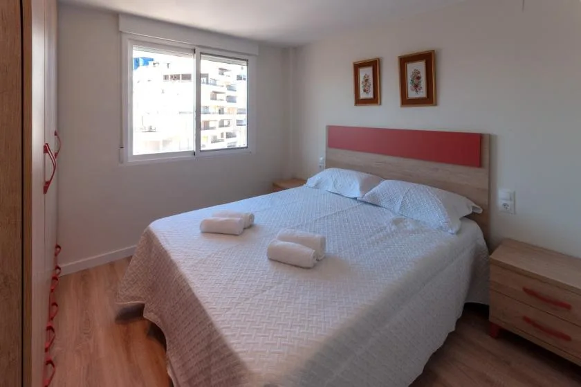 A bedroom with a double bed, bedside drawers, and a window.
