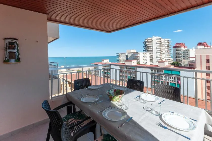A covered balcony dining area overlooks the sea and nearby buildings.