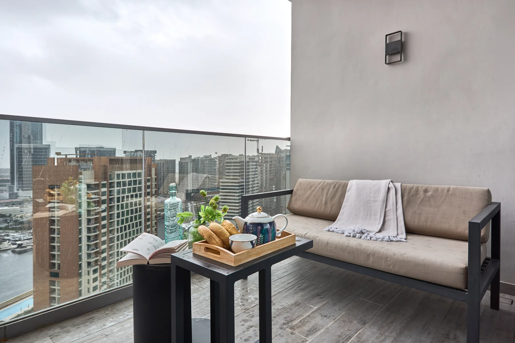 Una zona de estar en el balcón con una mesa baja mira hacia edificios de la ciudad.