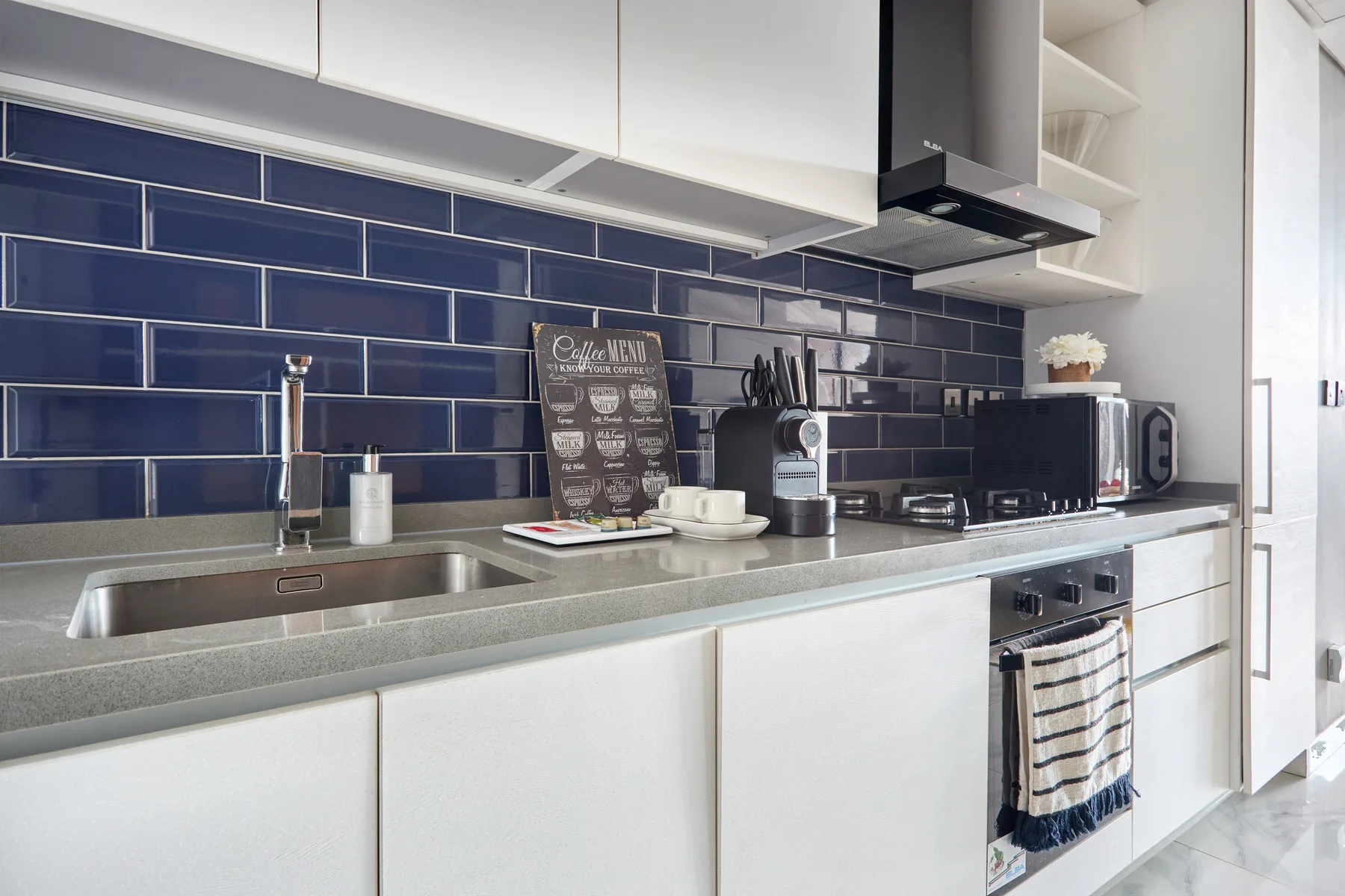 A modern kitchen with a long counter, sink, and dark tile backsplash.