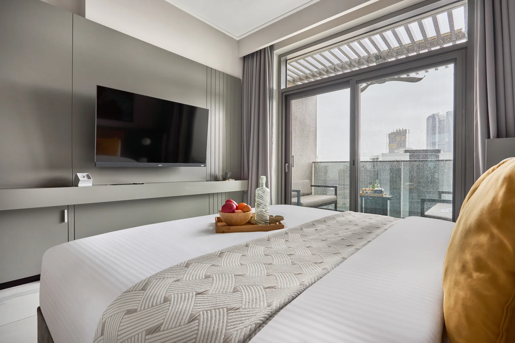 A bedroom with a neatly made bed and floor-to-ceiling windows overlooking the city.