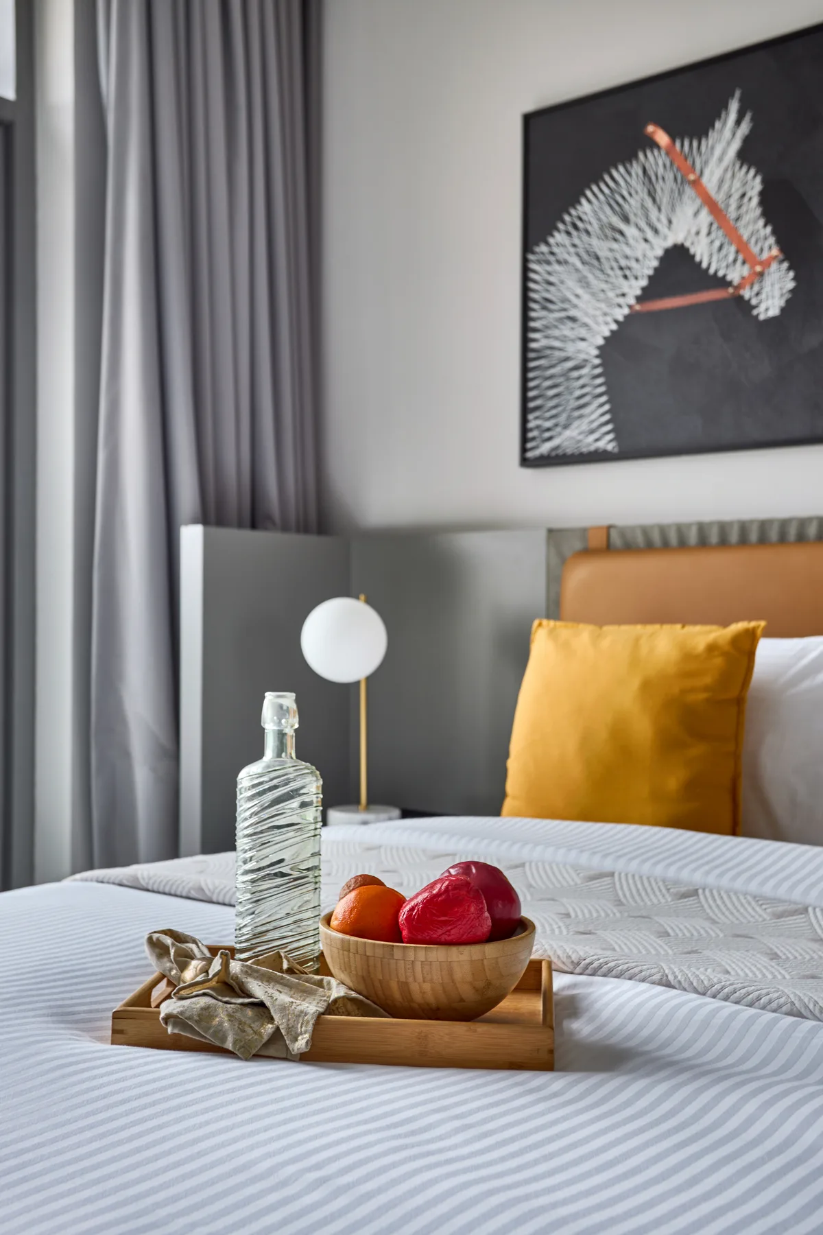 A neatly made bedroom bed with fruit on a tray and framed art above.