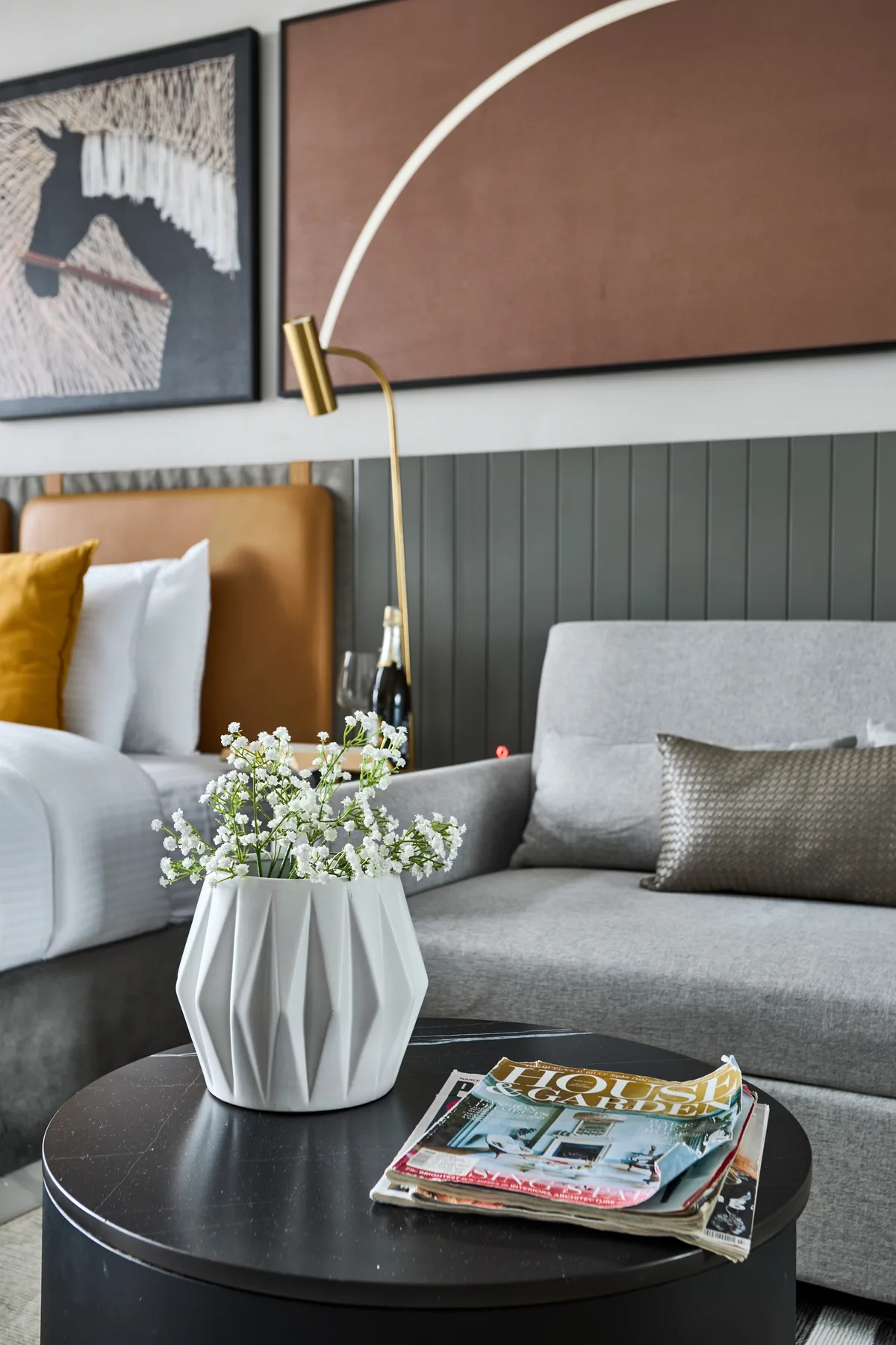 A bedroom seating area features a bed, gray sofa, and round coffee table.