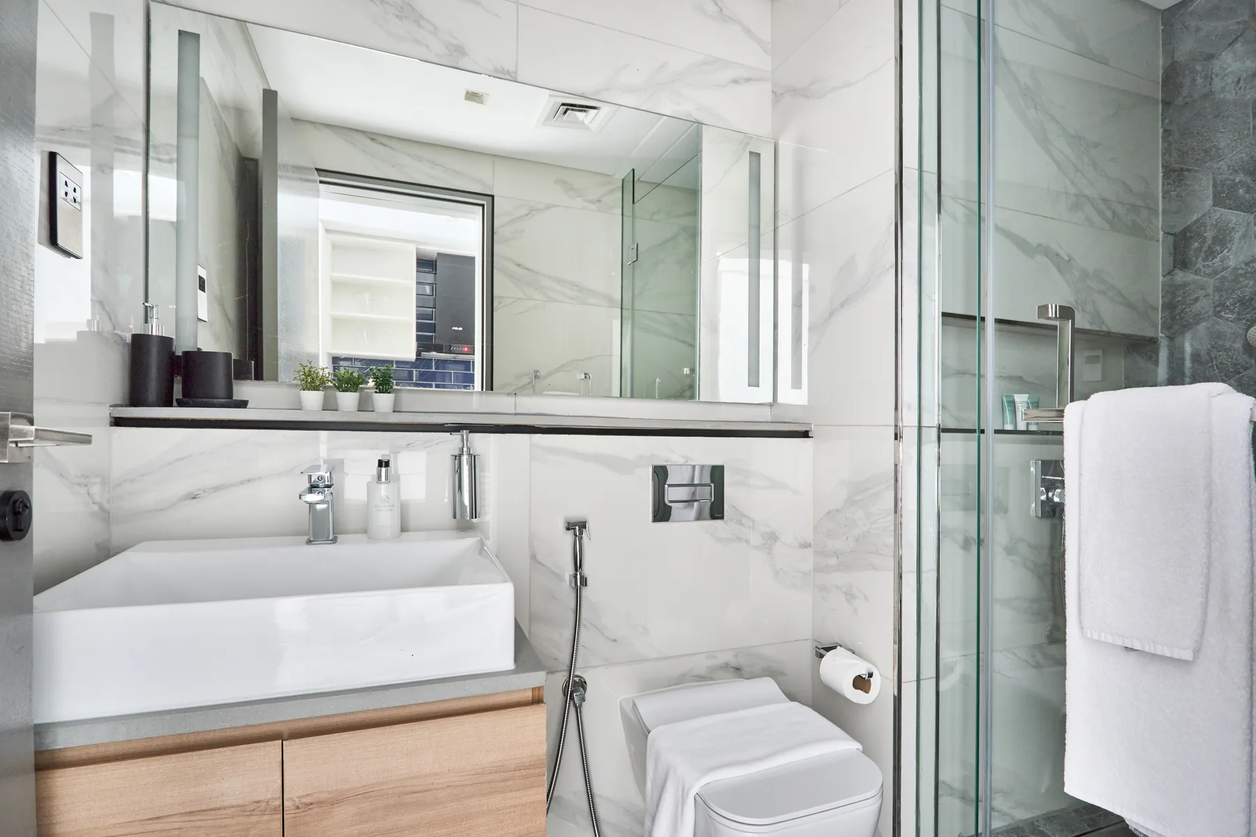 A bright bathroom with a wide mirror, sink, toilet, and glass shower.
