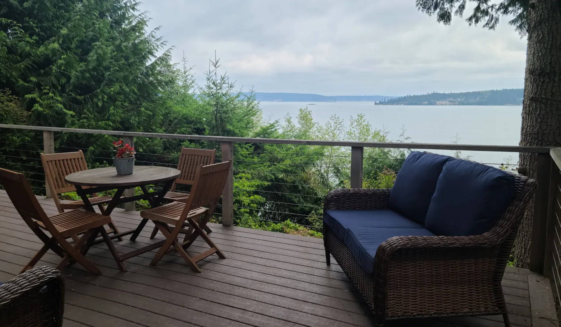 Una zona de descanso en una terraza mira hacia un lago, con una mesa y asientos acolchados.