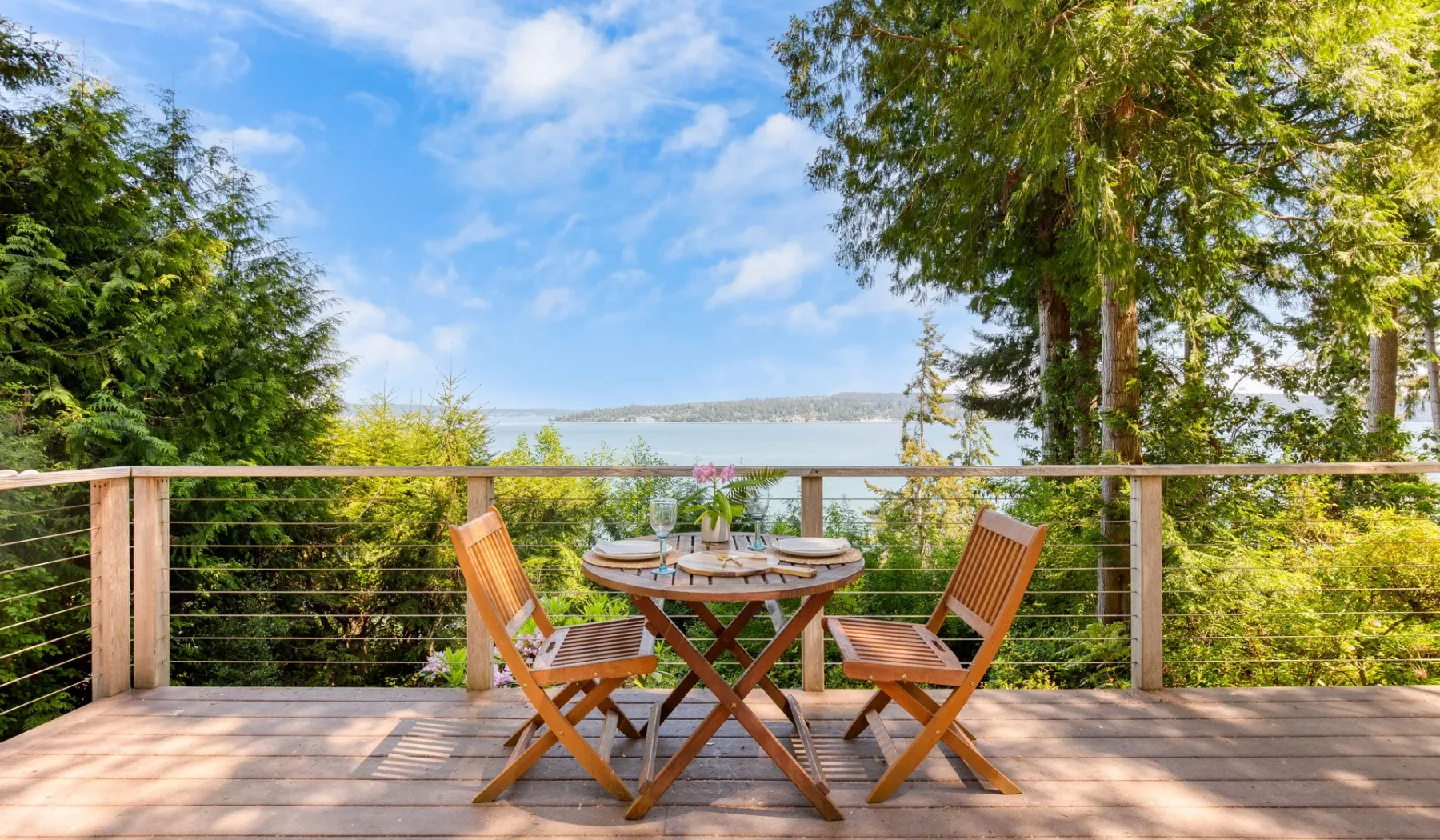 Una terraza de madera con asientos y una mesa al aire libre da al agua.