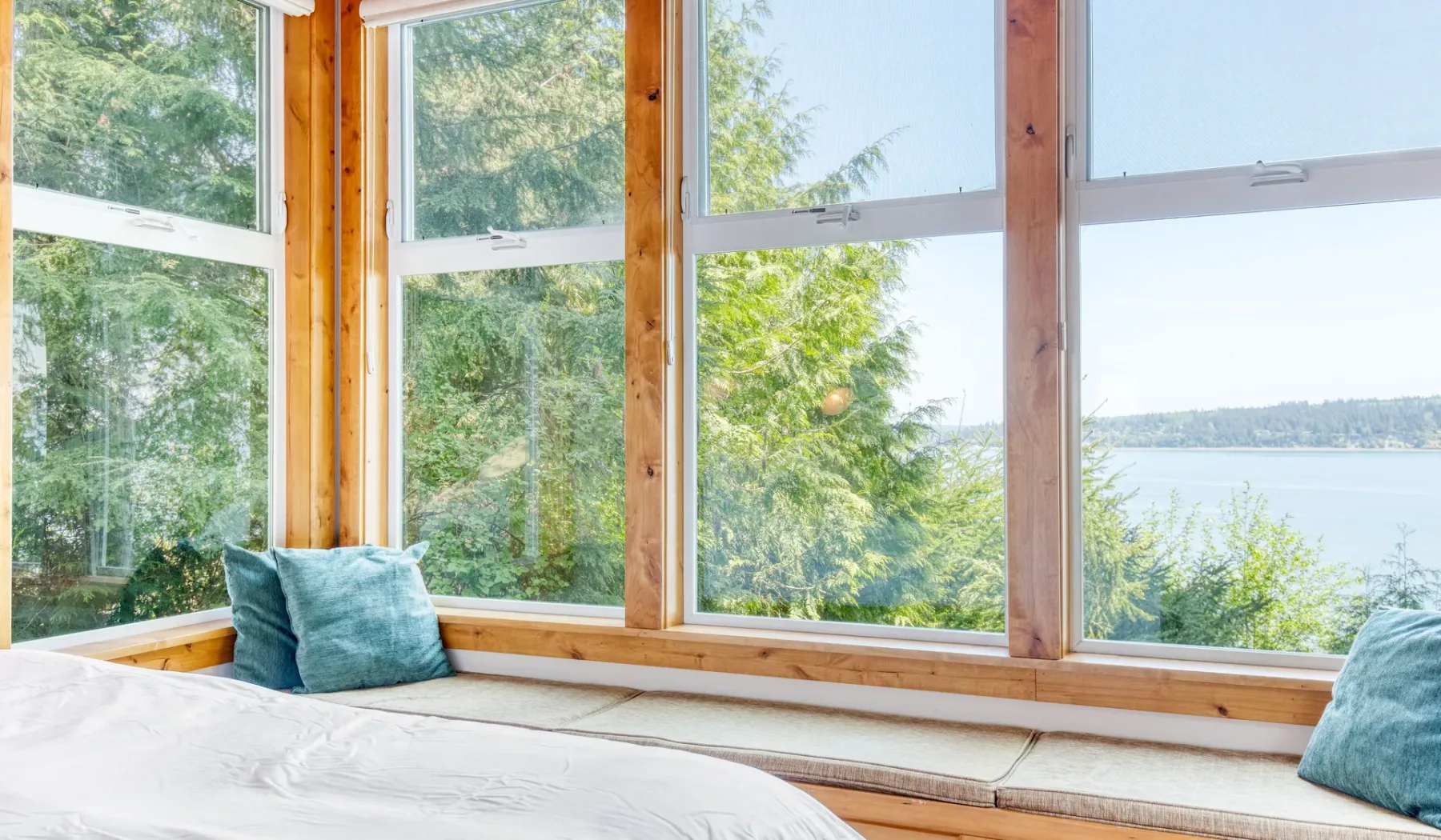 Una habitación luminosa con una cama junto a grandes ventanas con vistas al agua.